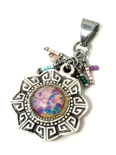 Circular silver pendant with a gear-like bezel, featuring a round opal shimmer focal bead and clusters of colorful seed beads and tiny pearls dangling below.